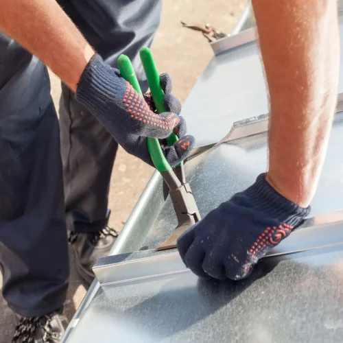 Roofer builder worker finishing folding a metal sheet using special pliers with a large flat grip