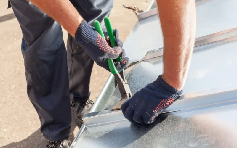 Roofer builder worker finishing folding a metal sheet Roofer builder worker finishing folding a metal sheet using special pliers with a large flat grip